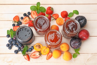 Photo of Tasty sweet jams in jars surrounded by ingredients on light wooden table, flat lay