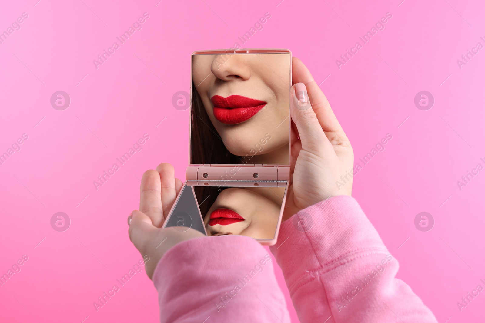 Beautiful woman with red lips looking in compact mirror on pink background, closeup Image of Beautiful woman with red lips looking in compact mirror on pink background, closeup