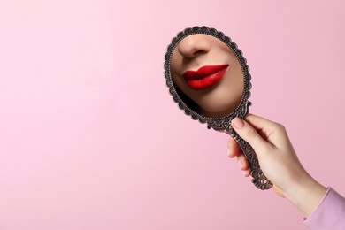 Image of Beautiful woman with red lips looking in handheld mirror on pink background, closeup