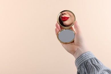 Image of Beautiful woman with red lips looking in compact mirror on beige background, closeup