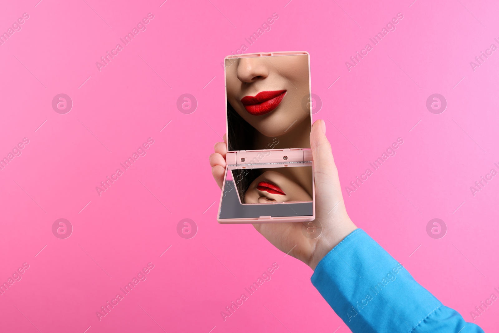 Beautiful woman with red lips looking in compact mirror on pink background, closeup Image of Beautiful woman with red lips looking in compact mirror on pink background, closeup