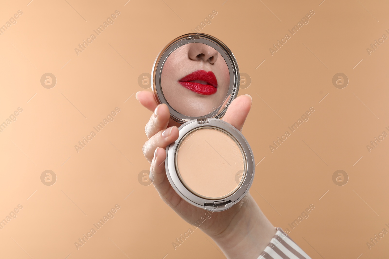 Beautiful woman with red lips looking in compact powder mirror on dark beige background, closeup Image of Beautiful woman with red lips looking in compact powder mirror on dark beige background, closeup