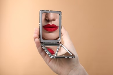 Image of Beautiful woman with red lips looking in compact mirror on dark beige background, closeup