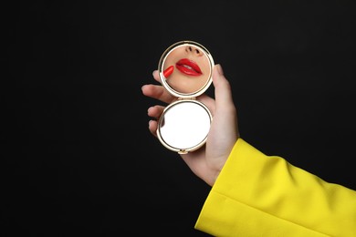 Image of Beautiful woman looking in compact mirror while applying red lipstick on black background, closeup