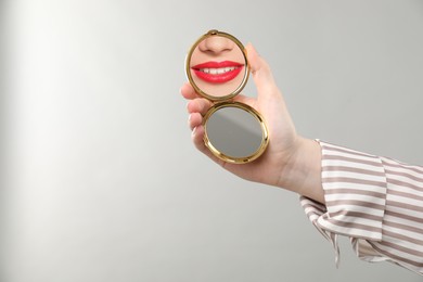 Image of Beautiful woman with red lips looking in compact mirror on light background, closeup