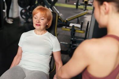Photo of Senior woman exercising under professional trainer's supervision in gym