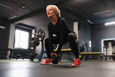 Photo of Senior woman training with kettlebell in gym, low angle view