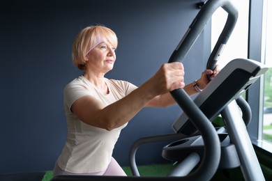 Photo of Senior woman training on elliptical machine in gym