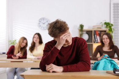 Photo of Bullying. Upset teenage boy and schoolmates pointing at him in classroom, selective focus
