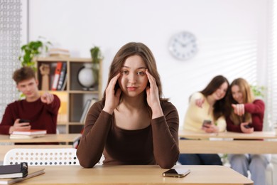 Photo of Cyber bullying. Upset teenage girl with smartphone and schoolmates pointing at her in classroom, selective focus