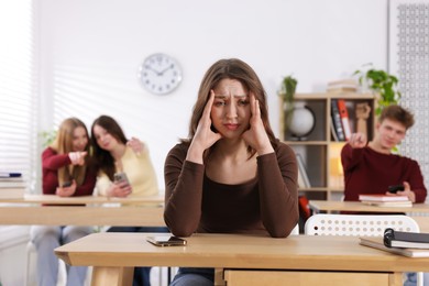 Photo of Cyber bullying. Upset teenage girl with smartphone and schoolmates pointing at her in classroom, selective focus