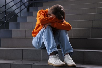 Photo of Bullying. Upset teenage girl on stairs indoors