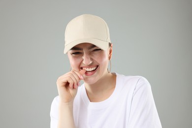 Photo of Smiling woman in stylish baseball hat on grey background, closeup