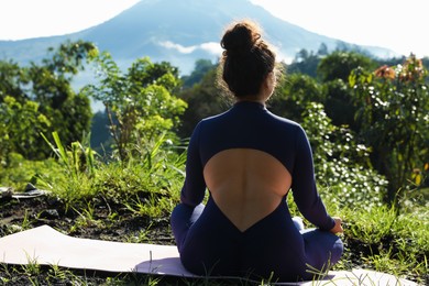 Photo of Woman meditating on yoga mat outdoors, back view