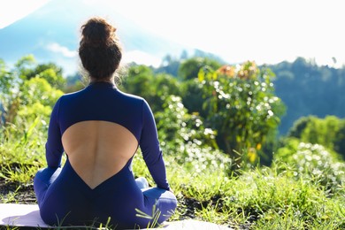 Photo of Woman meditating on yoga mat outdoors, back view. Space for text