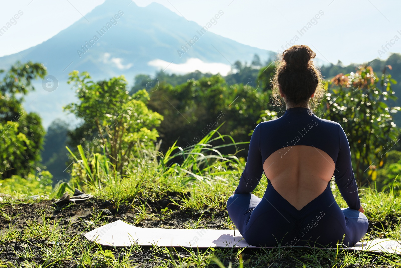 Photo of Woman meditating on yoga mat outdoors, back view. Space for text