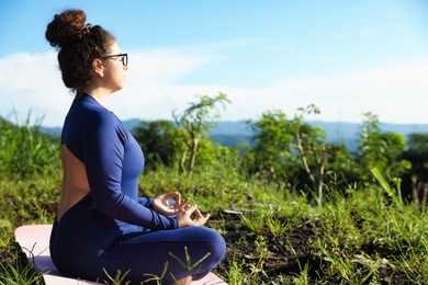Photo of Woman meditating on yoga mat outdoors. Space for text