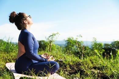 Photo of Woman meditating on yoga mat outdoors. Space for text