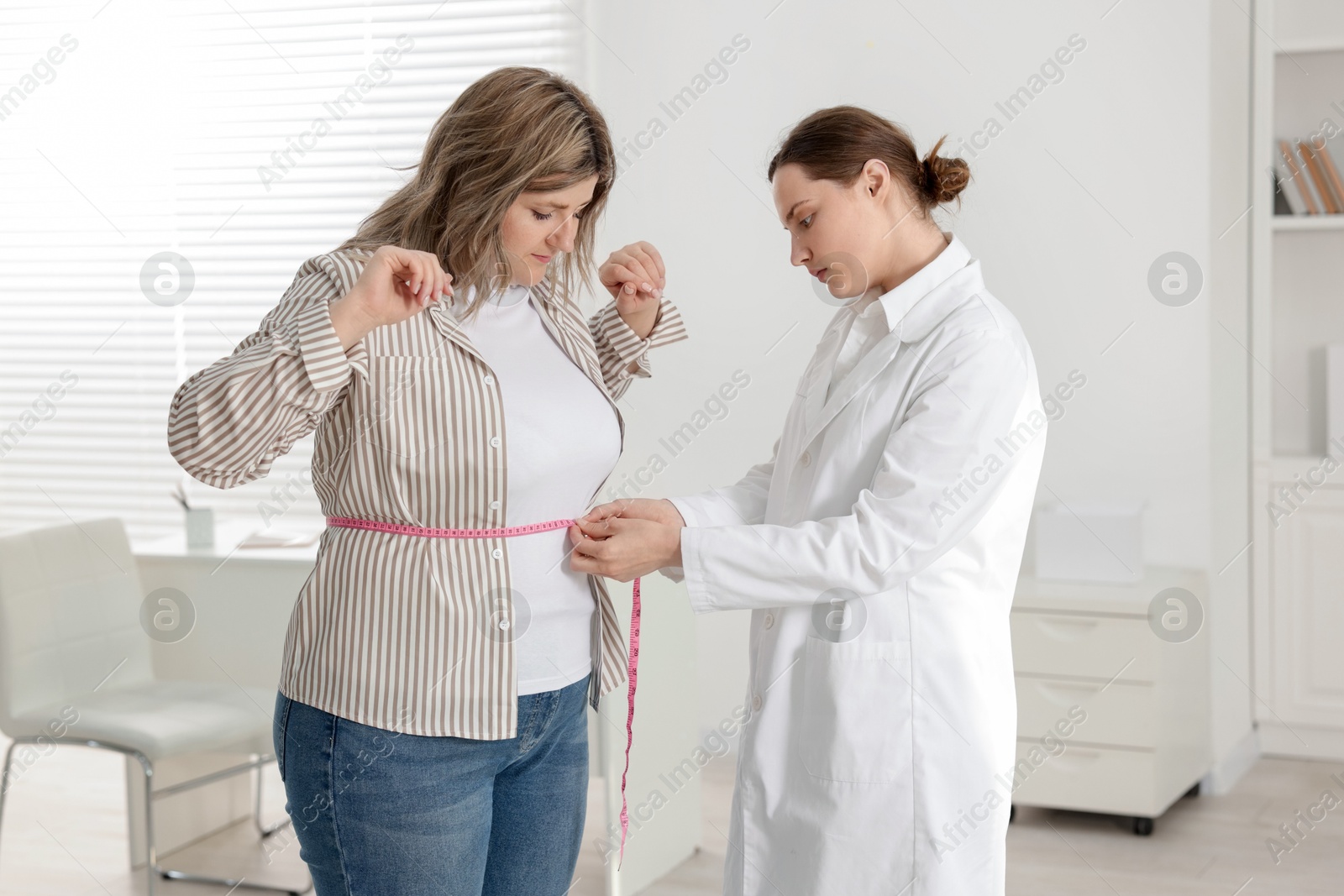 Weight loss. Nutritionist measuring overweight woman's waist with tape in clinic Photo of Weight loss. Nutritionist measuring overweight woman's waist with tape in clinic