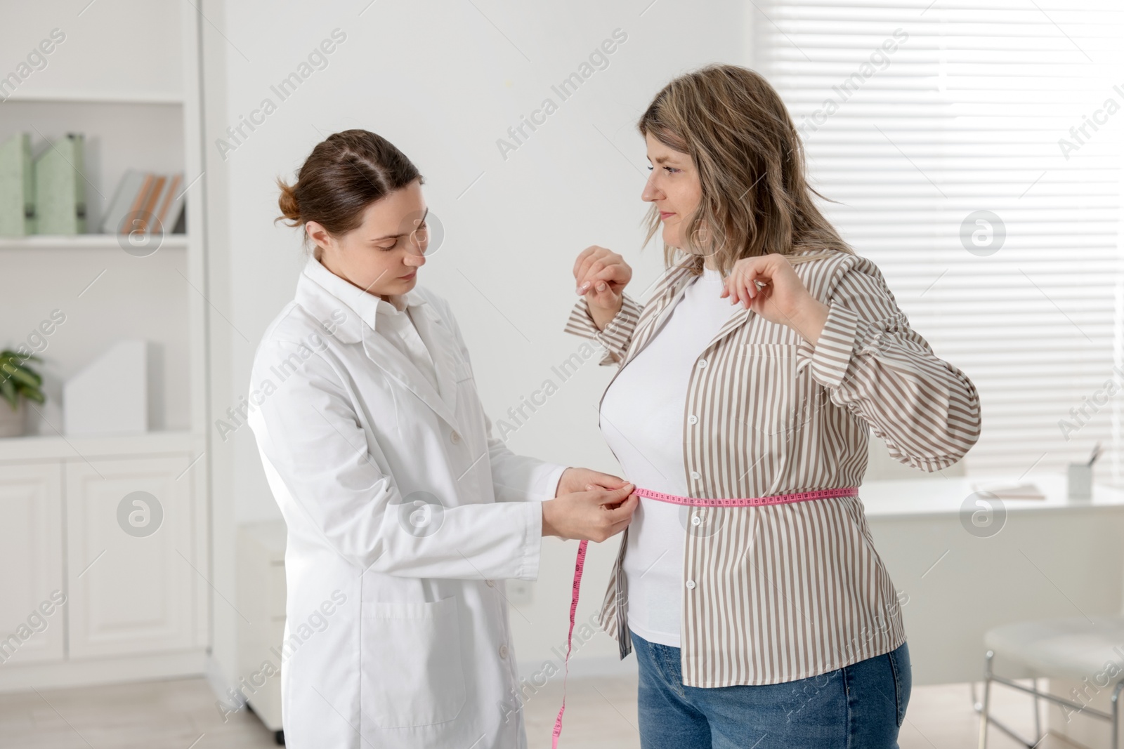 Weight loss. Nutritionist measuring overweight woman's waist with tape in clinic Photo of Weight loss. Nutritionist measuring overweight woman's waist with tape in clinic
