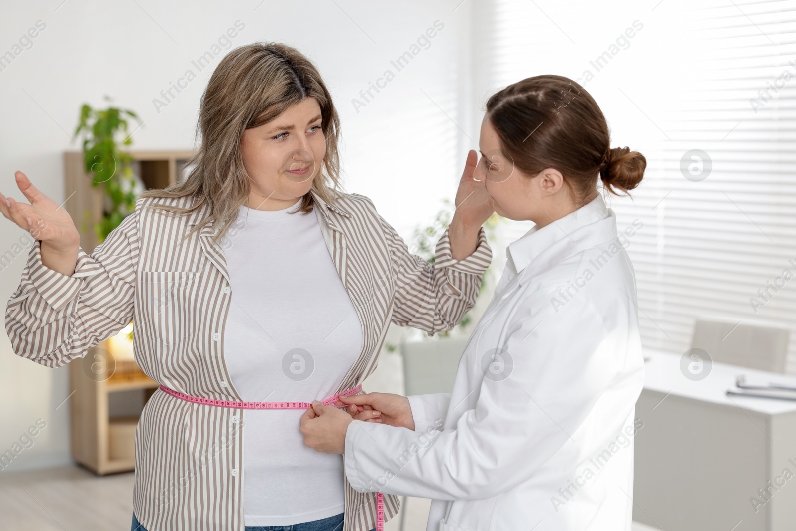 Weight loss. Nutritionist measuring overweight woman's waist with tape in clinic Photo of Weight loss. Nutritionist measuring overweight woman's waist with tape in clinic