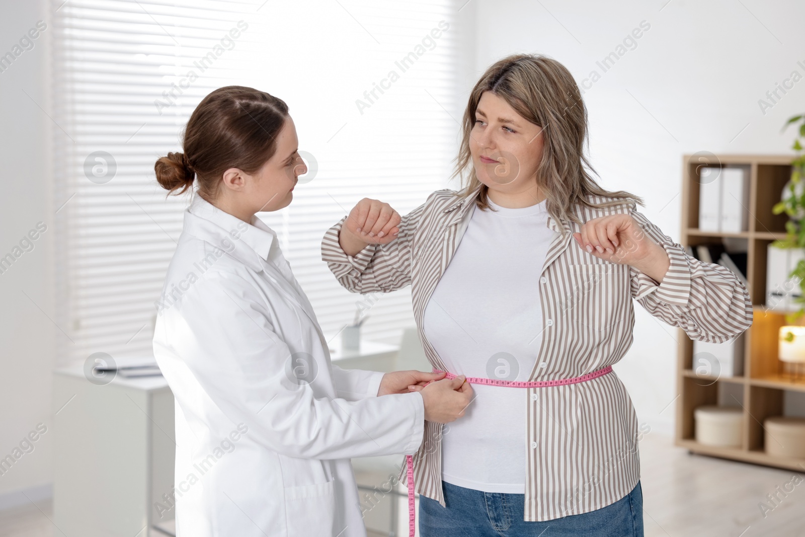Weight loss. Nutritionist measuring overweight woman's waist with tape in clinic Photo of Weight loss. Nutritionist measuring overweight woman's waist with tape in clinic