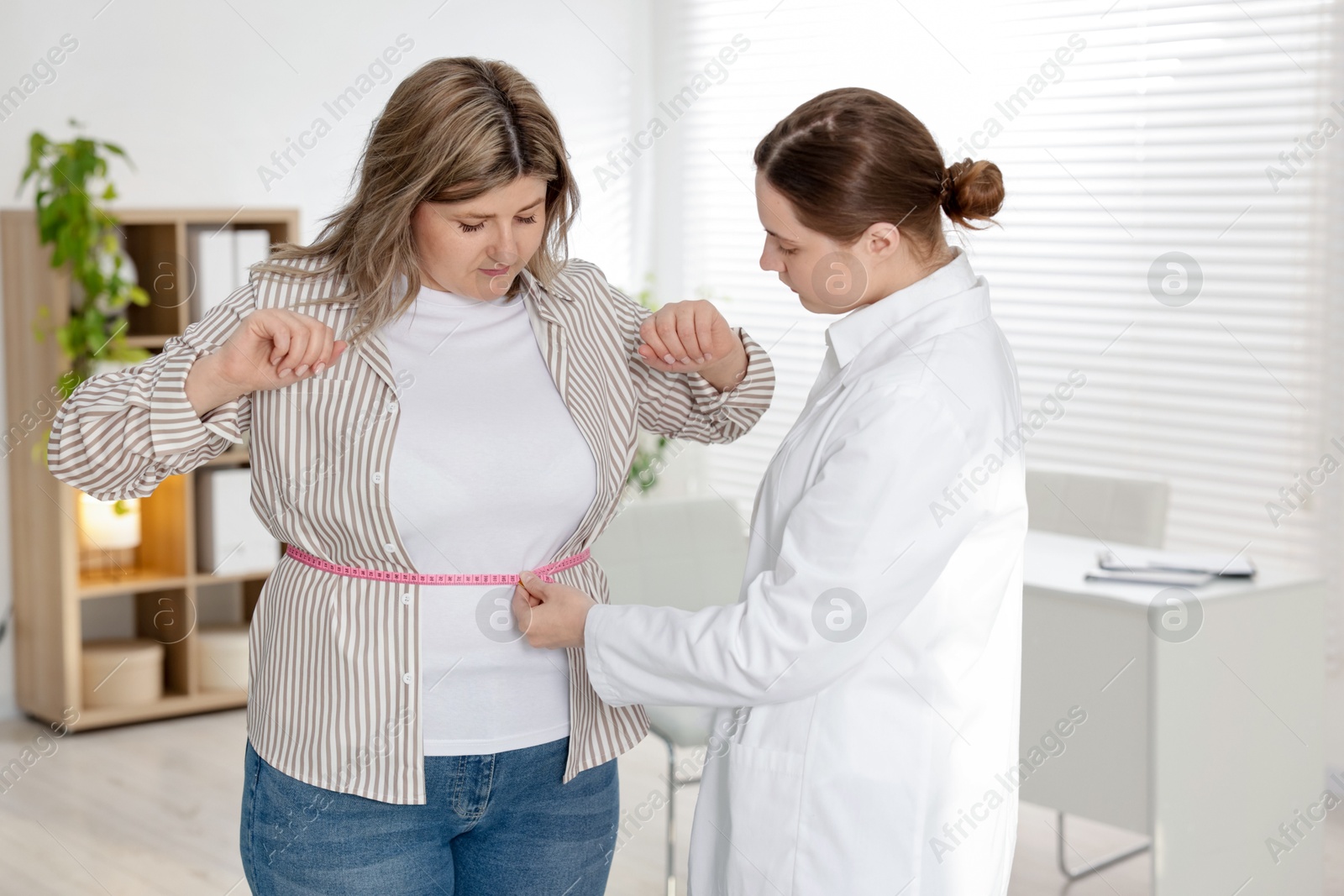 Photo of Weight loss. Nutritionist measuring overweight woman's waist with tape in clinic