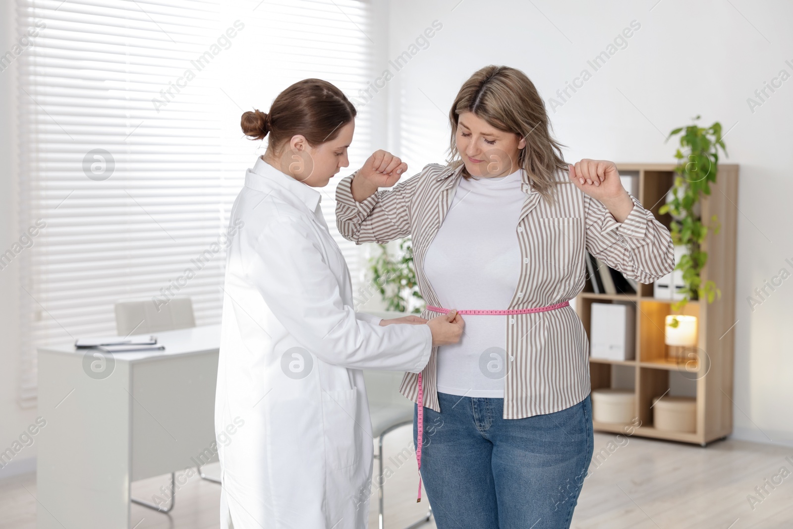 Photo of Weight loss. Nutritionist measuring overweight woman's waist with tape in clinic