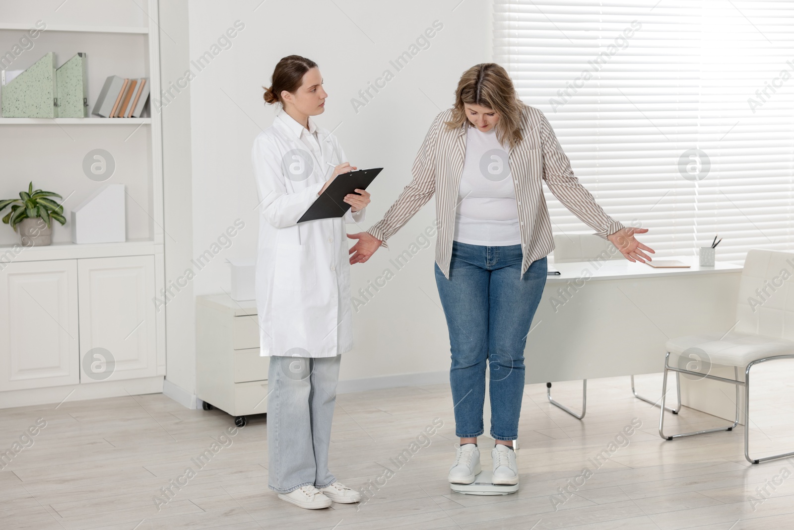 Weight loss. Overweight woman standing on scales during consultation with nutritionist in clinic Photo of Weight loss. Overweight woman standing on scales during consultation with nutritionist in clinic