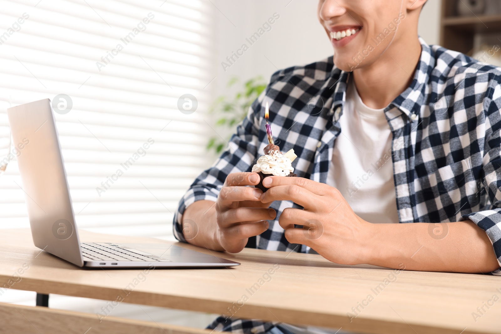 Birthday celebration. Man with cupcake having video call via laptop at table indoors, closeup Photo of Birthday celebration. Man with cupcake having video call via laptop at table indoors, closeup