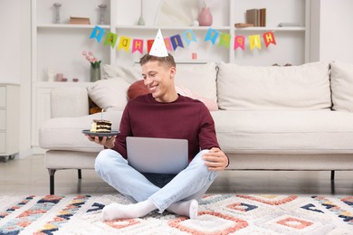 Photo of Man with piece of cake celebrating his birthday and having video call via laptop at home