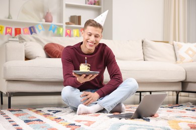Photo of Man with piece of cake celebrating his birthday and having video call via laptop at home