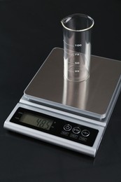Photo of Scale with empty beaker on black mirror table, closeup
