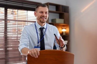 Photo of Man giving public speech with microphone at lectern indoors