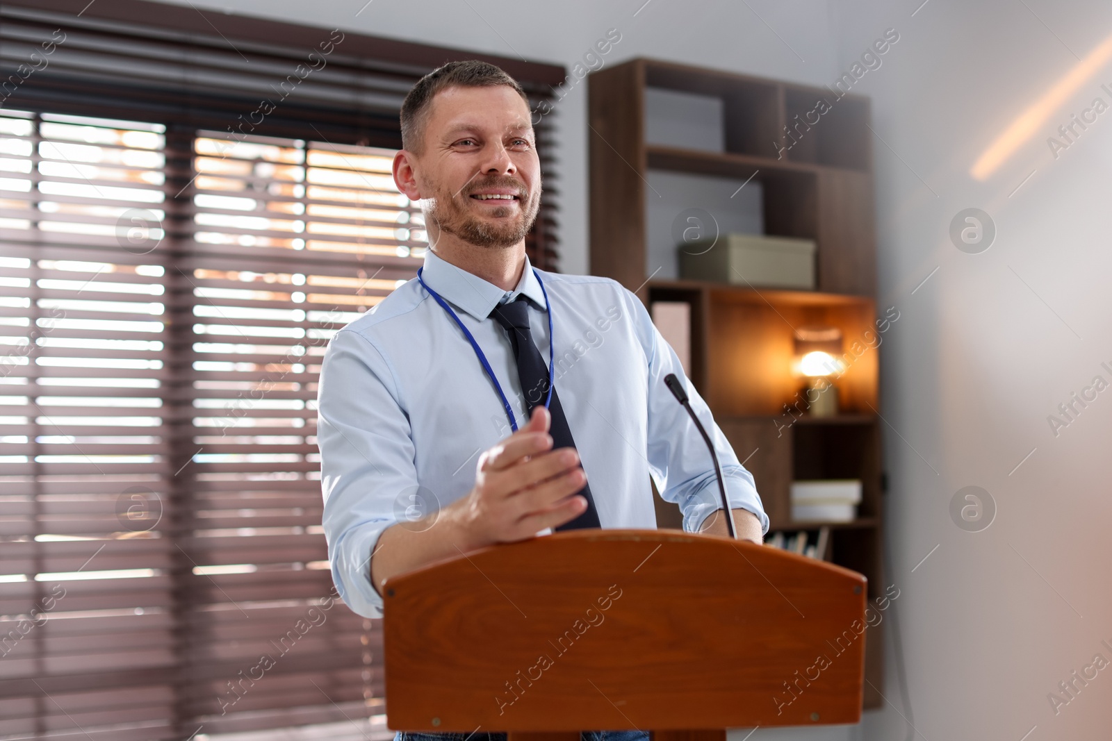 Man giving public speech with microphone at lectern indoors Photo of Man giving public speech with microphone at lectern indoors