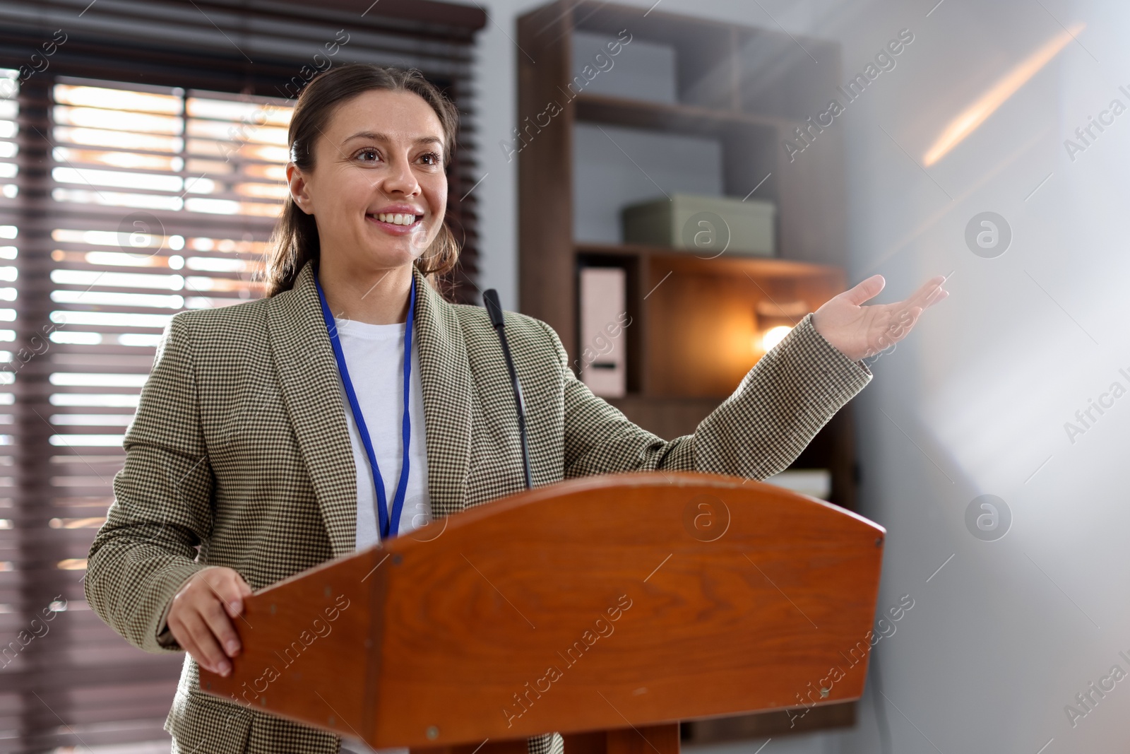 Woman giving public speech with microphone at lectern indoors Photo of Woman giving public speech with microphone at lectern indoors