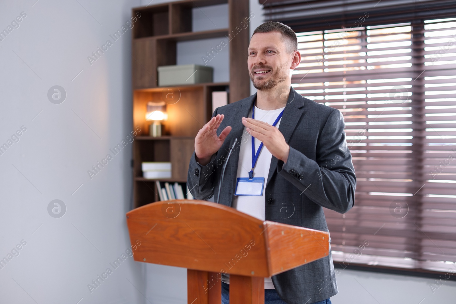Man giving public speech with microphone at lectern indoors Photo of Man giving public speech with microphone at lectern indoors