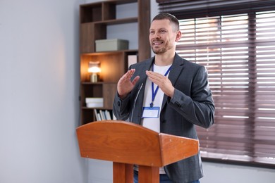 Photo of Man giving public speech with microphone at lectern indoors