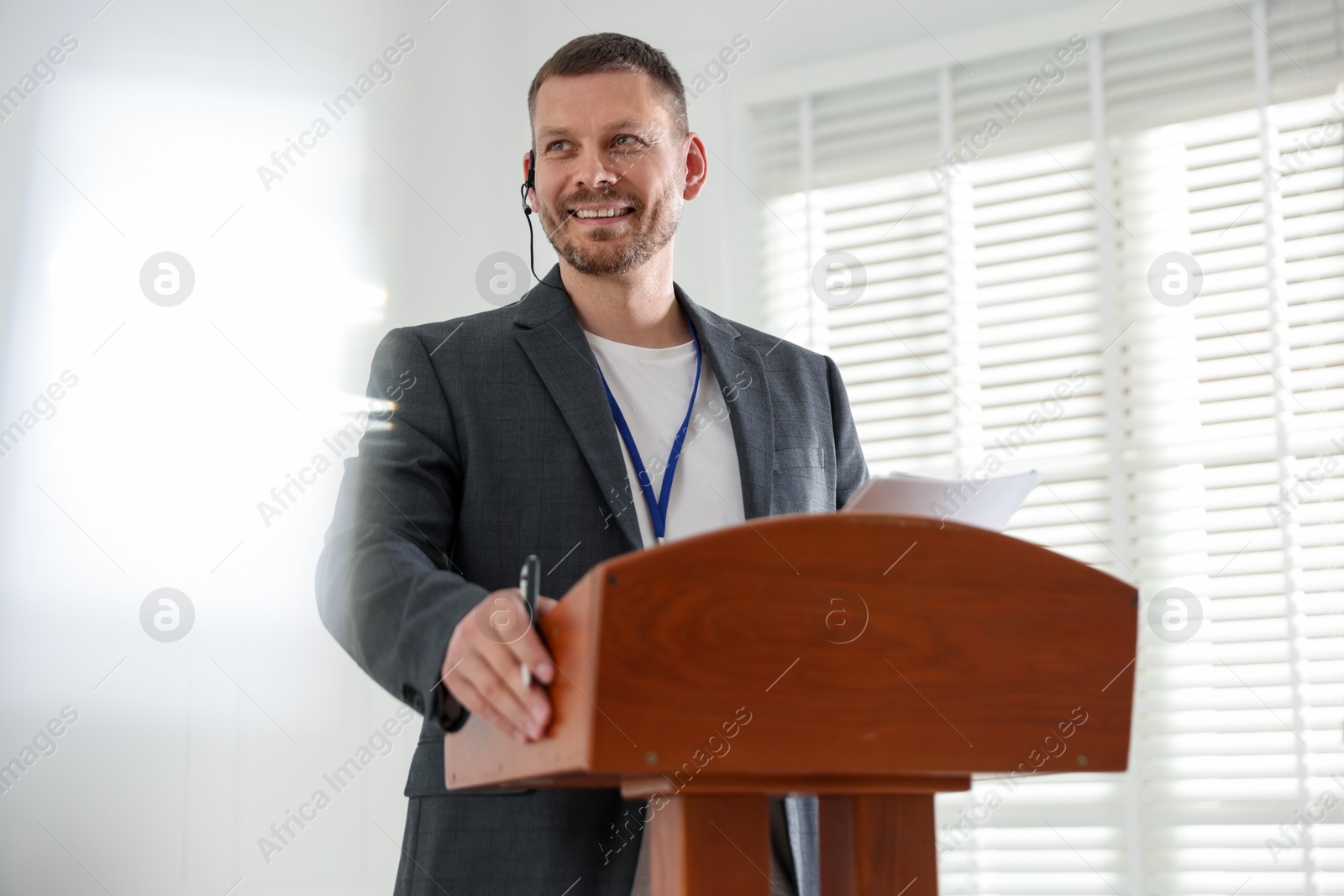 Man giving public speech with microphone at lectern indoors Photo of Man giving public speech with microphone at lectern indoors
