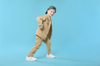 Photo of Happy little boy in baseball hat dancing on light blue background