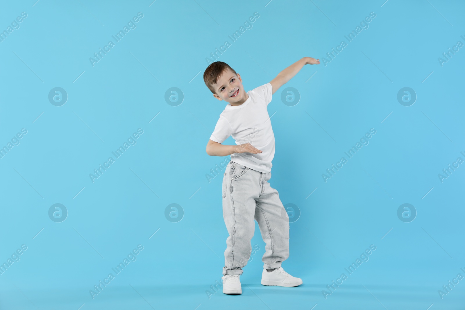 Happy little boy dancing on light blue background Photo of Happy little boy dancing on light blue background