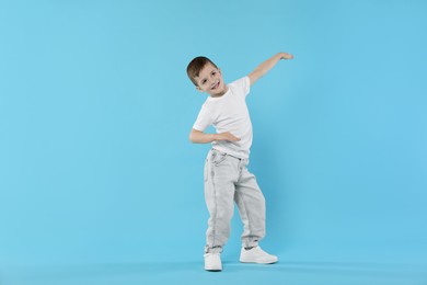 Photo of Happy little boy dancing on light blue background