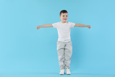Photo of Happy little boy dancing on light blue background