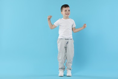 Photo of Happy little boy dancing on light blue background. Space for text