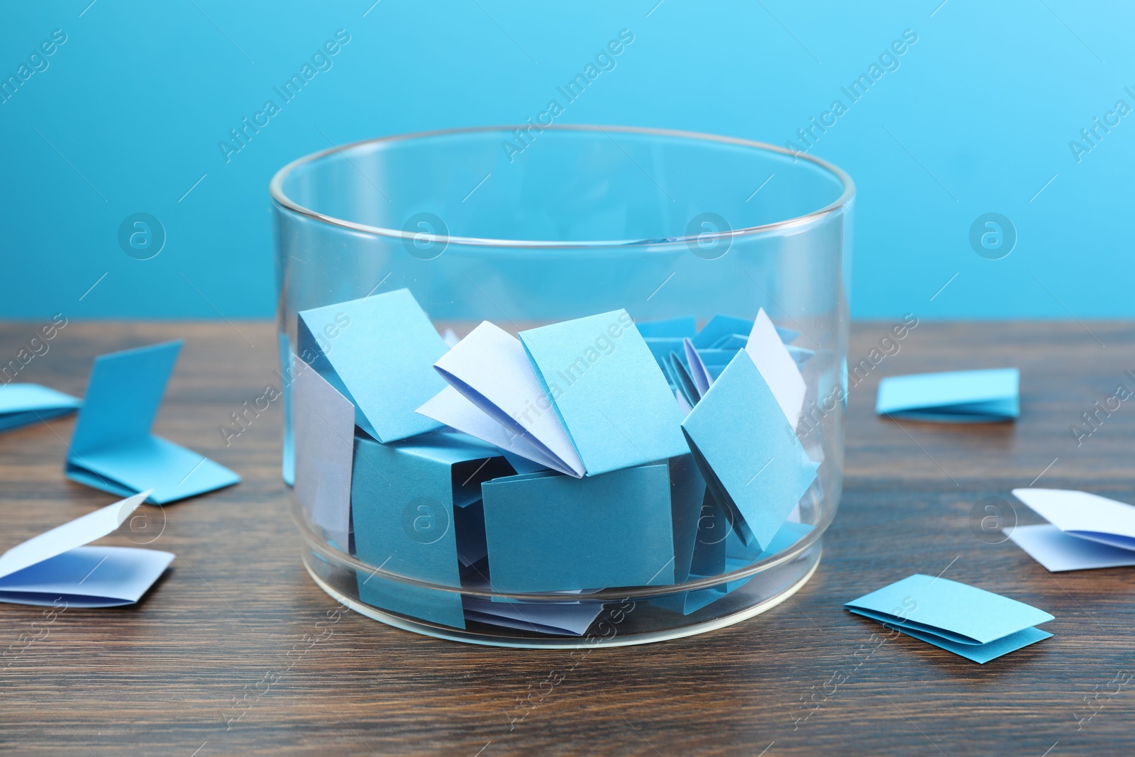 Colorful paper pieces in glass jar on wooden table against light blue background, closeup Photo of Colorful paper pieces in glass jar on wooden table against light blue background, closeup