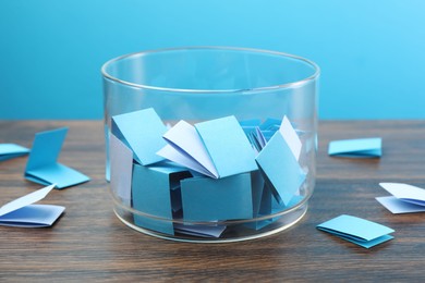 Photo of Colorful paper pieces in glass jar on wooden table against light blue background, closeup