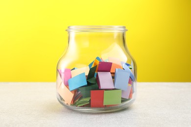 Photo of Jar with colorful pieces of paper on light table against yellow background