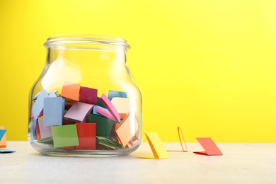 Photo of Jar with colorful pieces of paper on light table against yellow background. Space for text