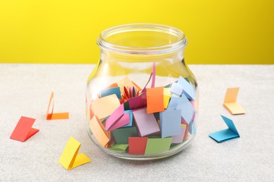Photo of Jar with colorful pieces of paper on light table against yellow background