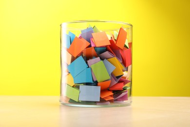 Photo of Jar with colorful pieces of paper on wooden table against yellow background